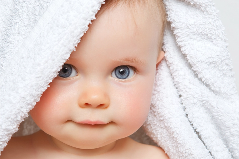 baby with big blue eyes wrapped in a towel