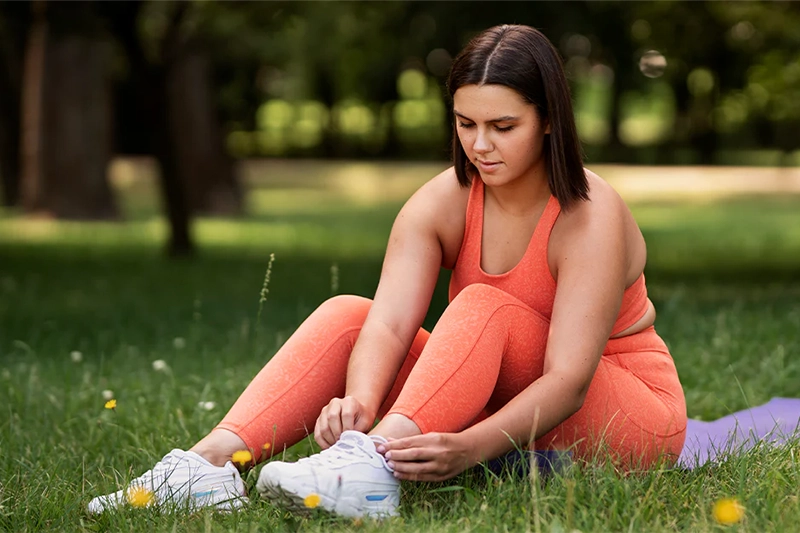 women sitting in grass, tying her tennis shoes before exercising to help combat her PCOS symptoms